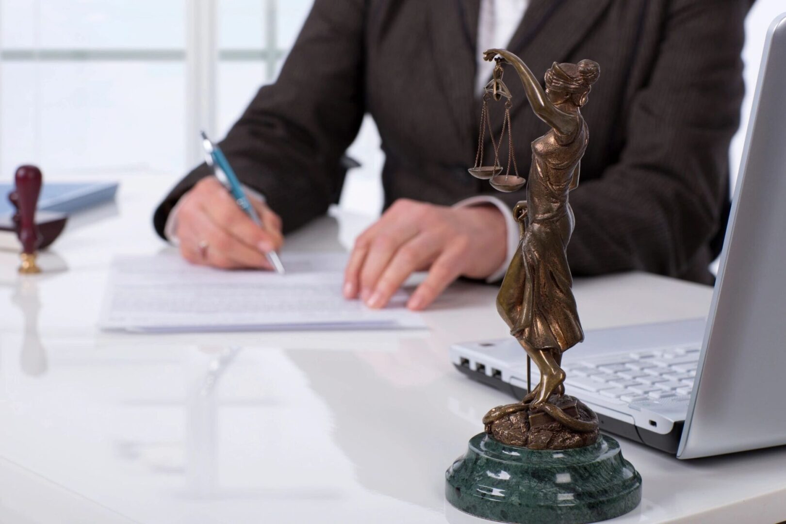 A man in suit and tie writing on paper next to statue of lady justice.