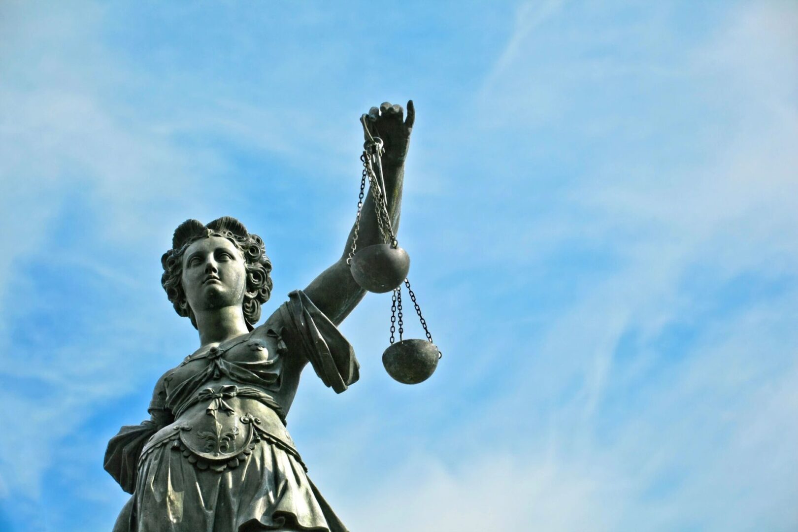 A statue of lady justice holding the balance in front of a blue sky.