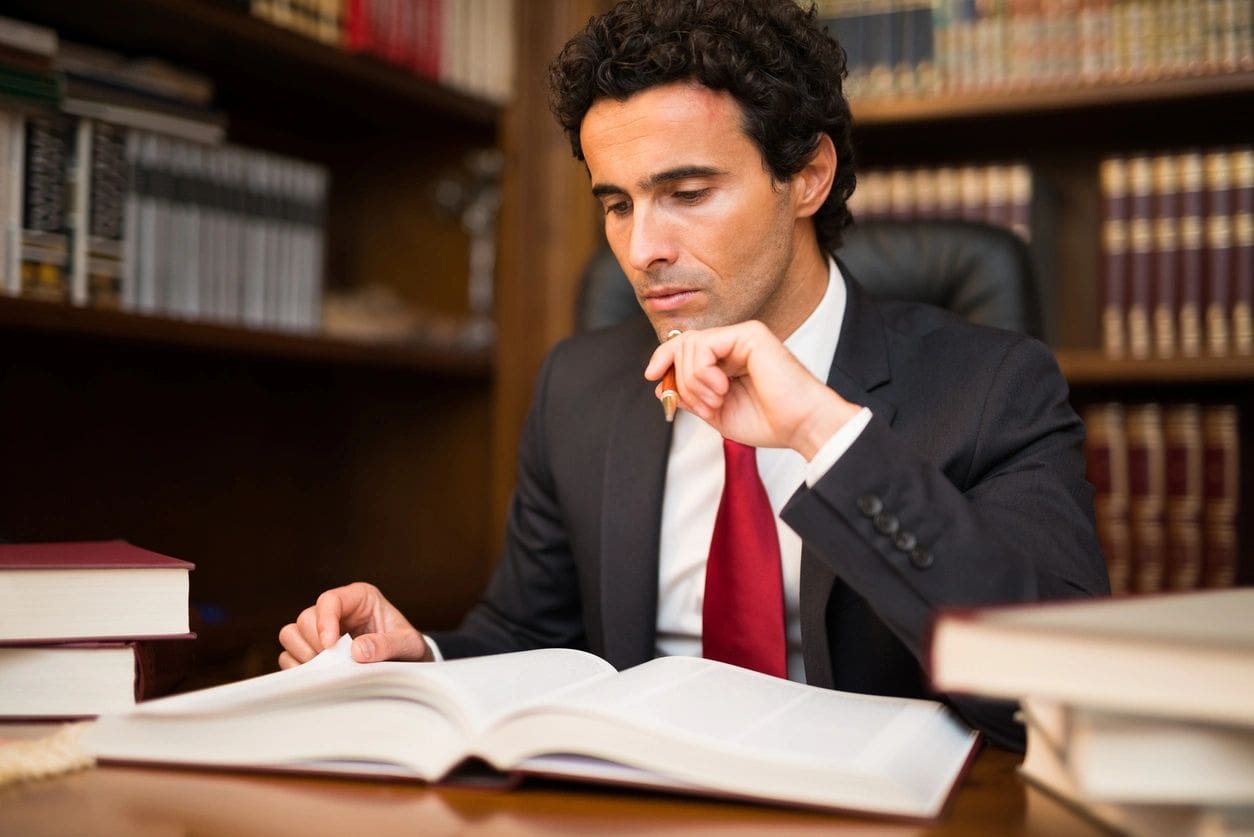 A man in suit and tie sitting at desk with book.