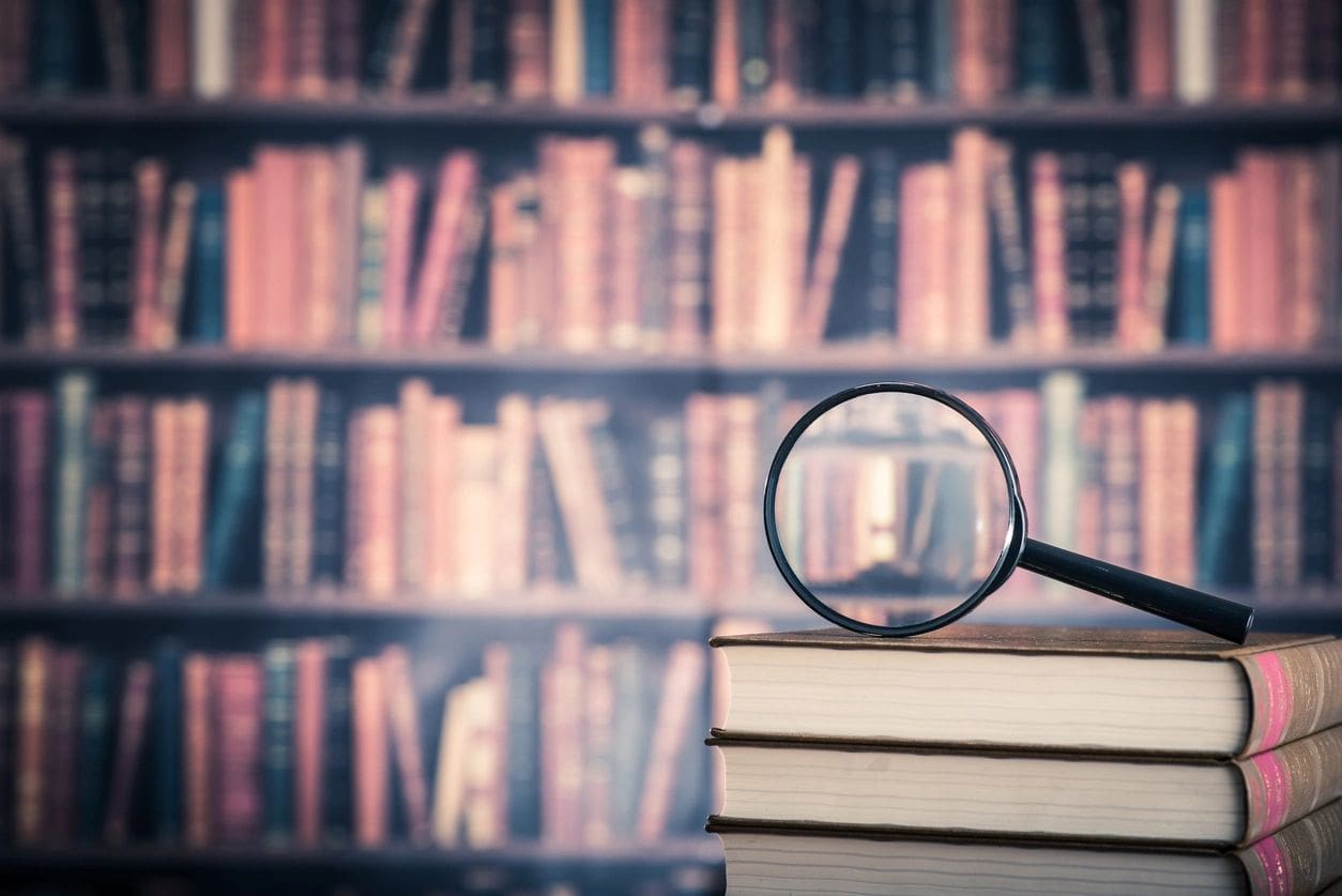 A stack of books with a magnifying glass on top.