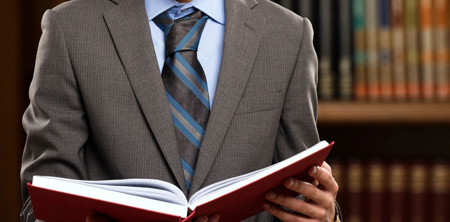 A man in suit and tie holding an open book.