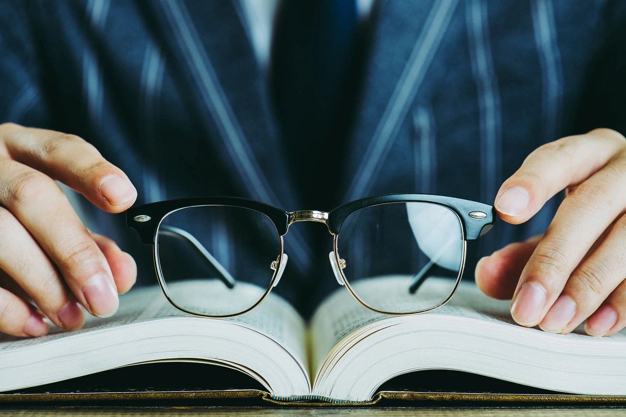 A person holding glasses over an open book.