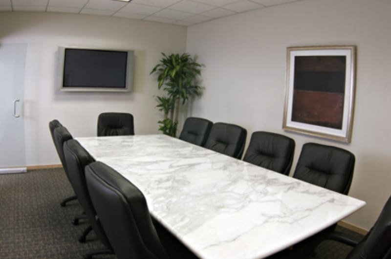 A large conference table with black chairs in front of a television.