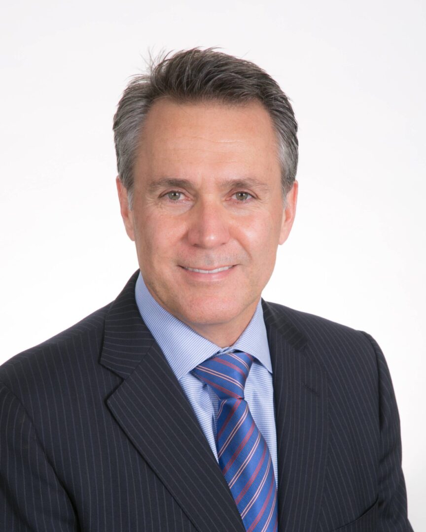 A man in a suit and tie standing up against a white wall.