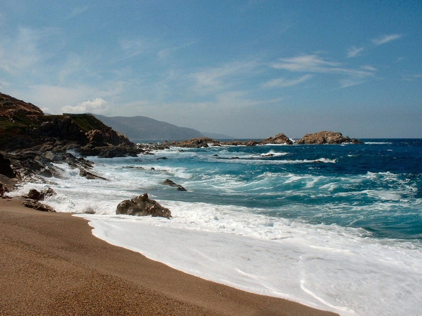 A beach with waves crashing on it and rocks in the background.